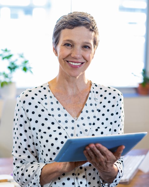 elderly-woman-with-an-Ipad-happily-smiling-in-front-of-the-window